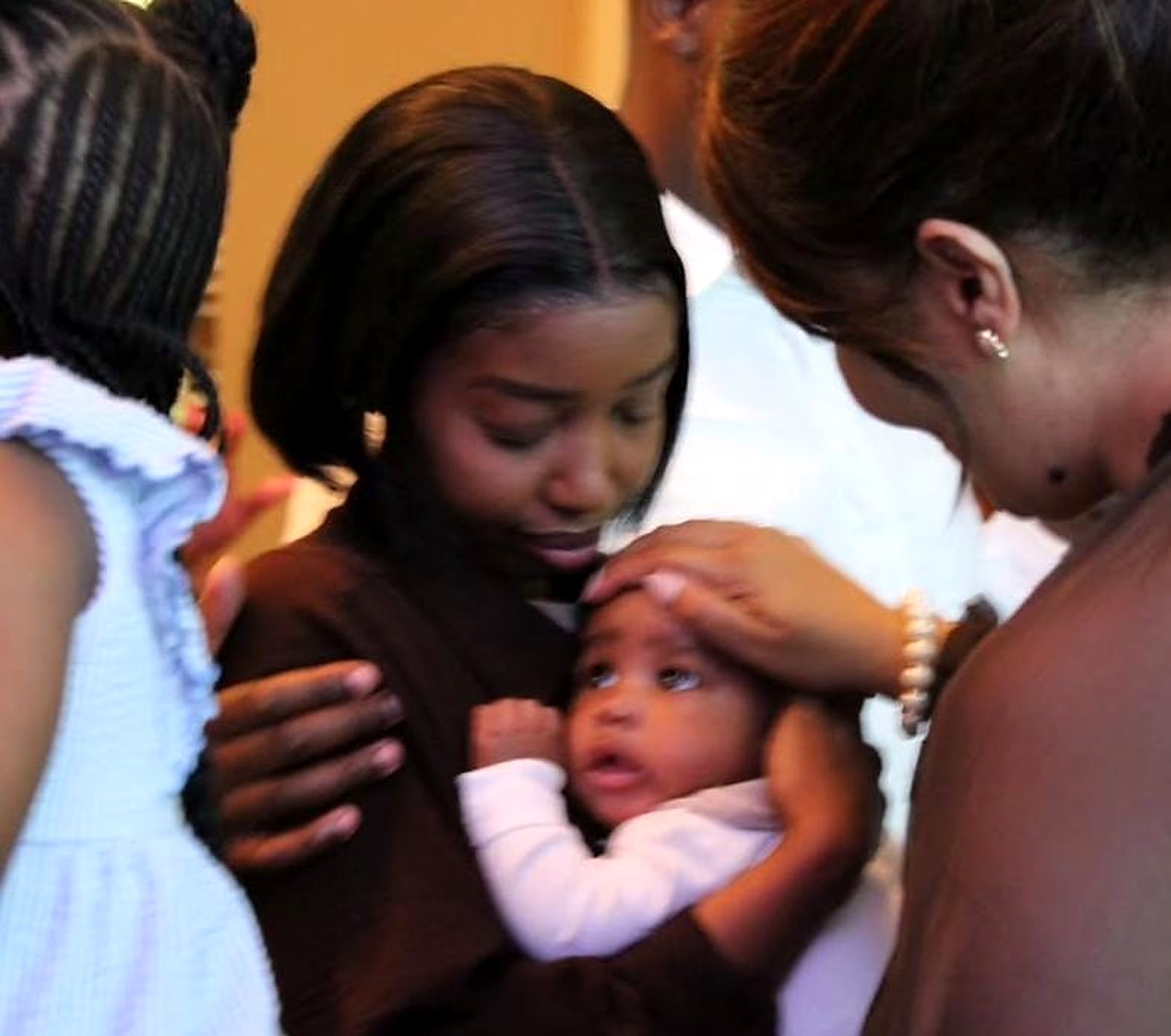 A big sister holding her baby brother as a mother prays a blessing during child dedication